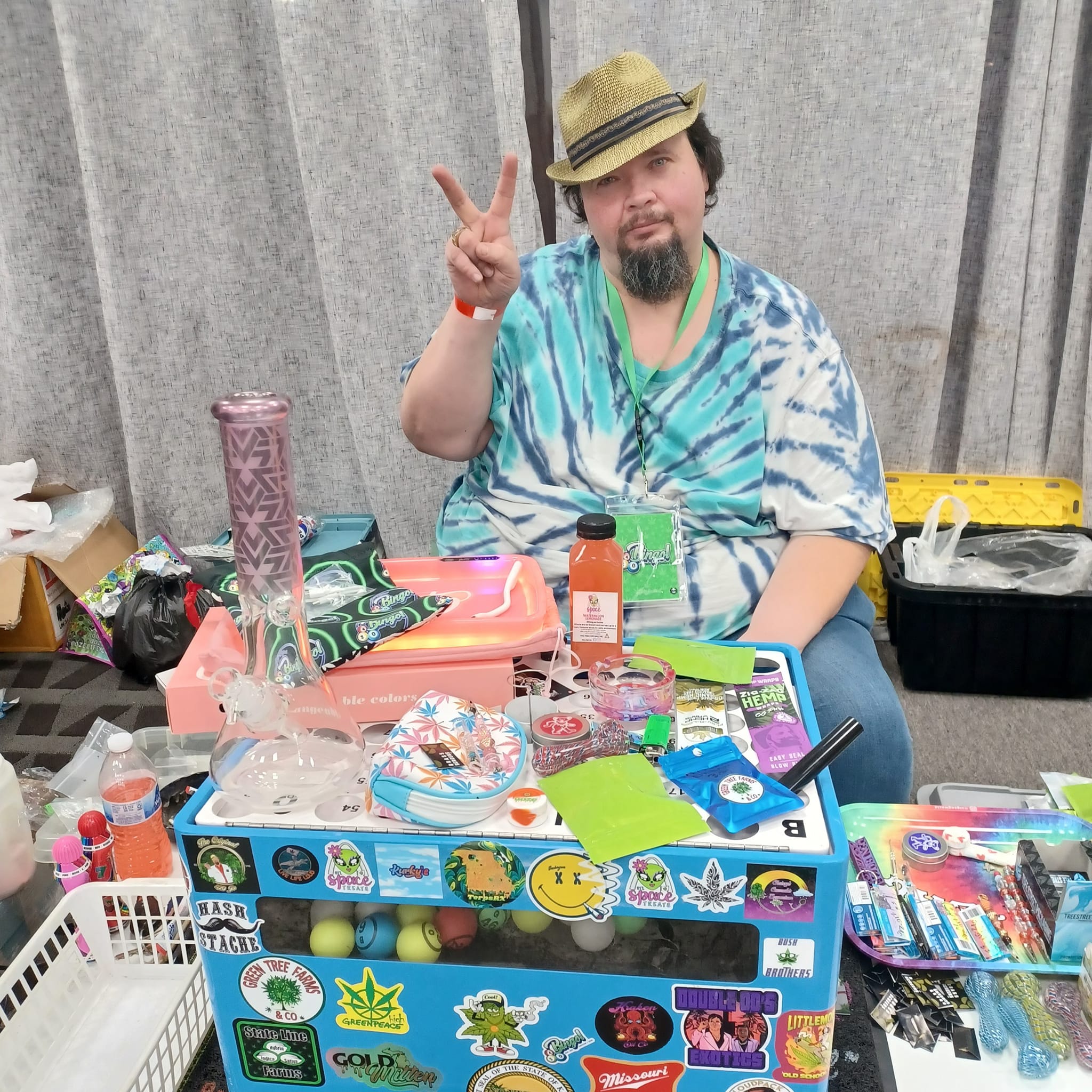 Person sitting at a colorful table with various items, giving a peace sign.