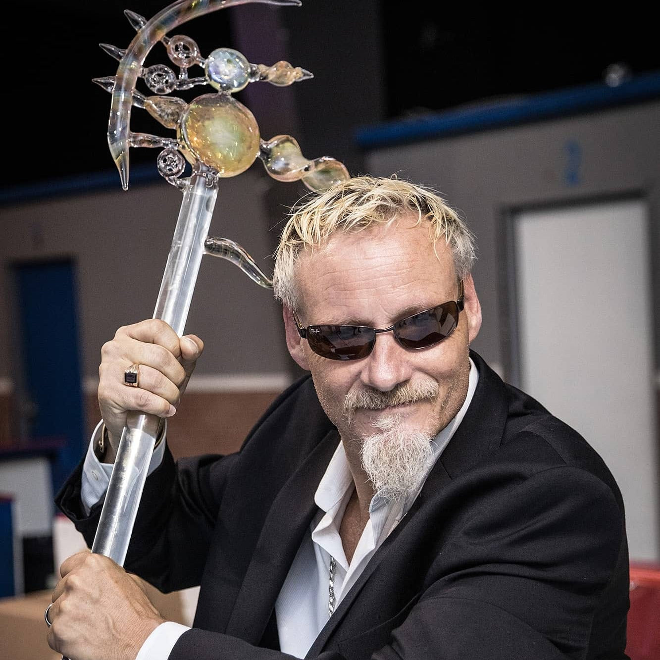 Uncle Stoner holding a decorative staff with intricate designs, wearing sunglasses and a black suit.